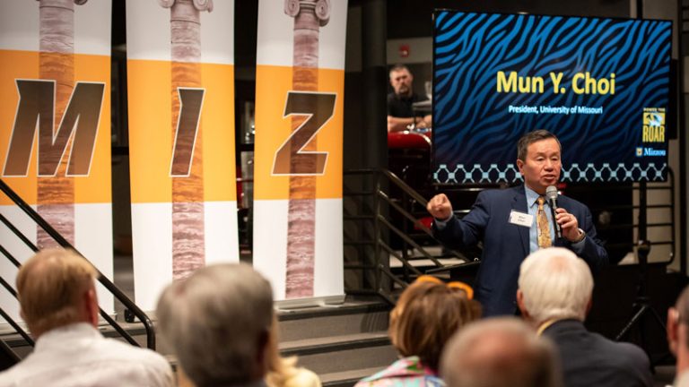 President Mun Y. Choi speaks to guests in front of banners displaying columns and the letters M, I and Z