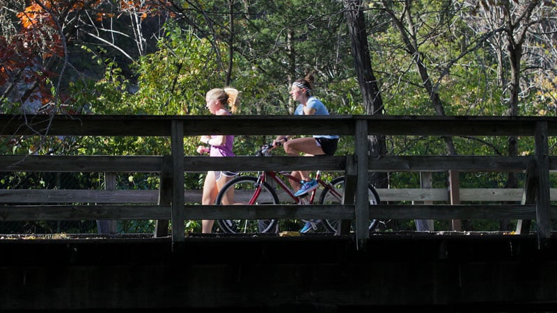 A jogger and a cyclist cross a wooden footbridge along the MKT Trail.