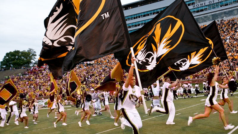 Cheerleaders carrying flags displaying Mizzou logos run across Faurot Field.