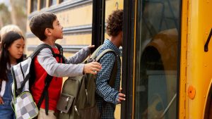 Elementary school children wearing backpacks board a school bus.