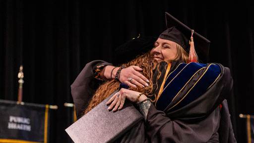 A Mizzou student holding a diploma hugs a faculty member during commencement.