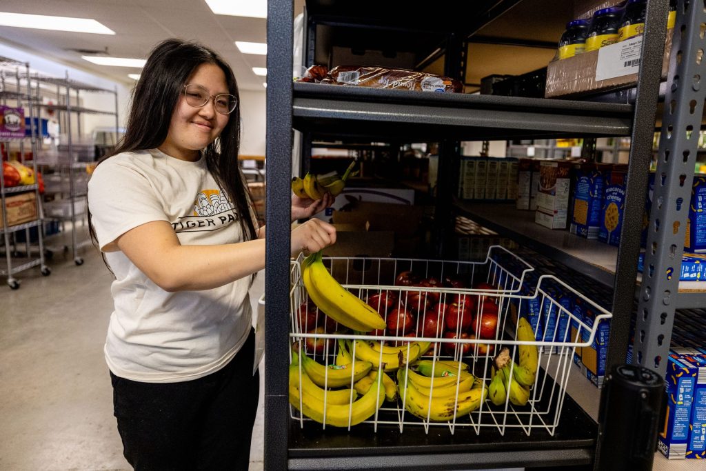A student volunteer fills a food bin with bananas at Tiger Pantry.